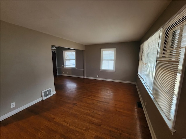 empty room with dark wood-type flooring, visible vents, and baseboards