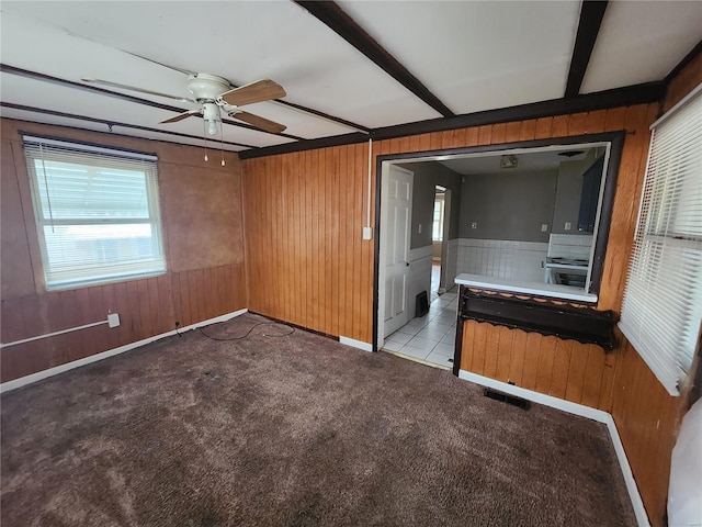 interior space with ceiling fan, wooden walls, light carpet, and beam ceiling