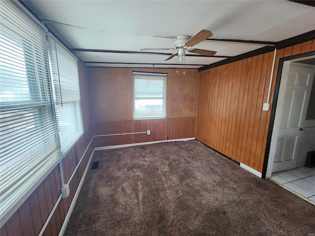 empty room featuring a ceiling fan, visible vents, dark carpet, and wood walls