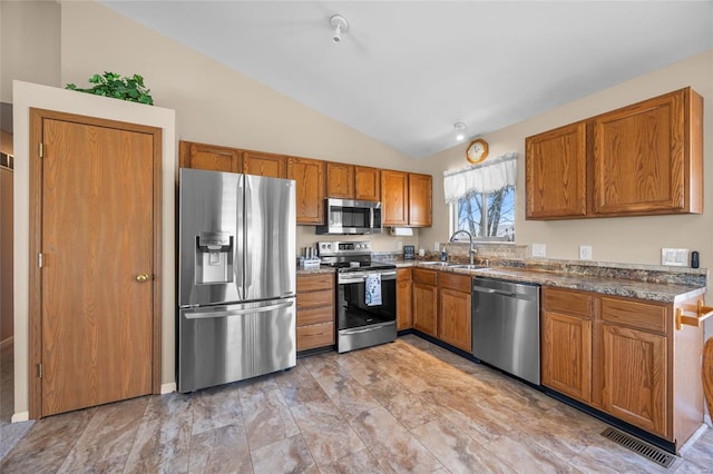 kitchen featuring visible vents, a sink, stainless steel appliances, brown cabinetry, and vaulted ceiling