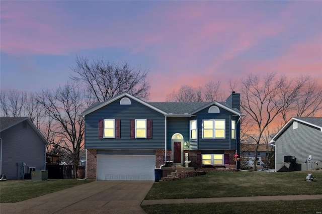 bi-level home featuring brick siding, concrete driveway, a chimney, a yard, and an attached garage