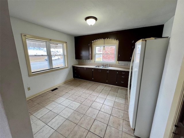 kitchen featuring decorative backsplash, dark brown cabinets, white fridge, and light tile patterned floors