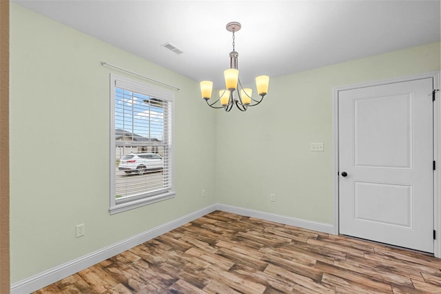 unfurnished dining area with wood-type flooring and a chandelier