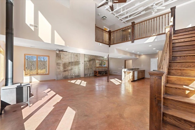 living room with a high ceiling, concrete floors, ceiling fan, and a wood stove