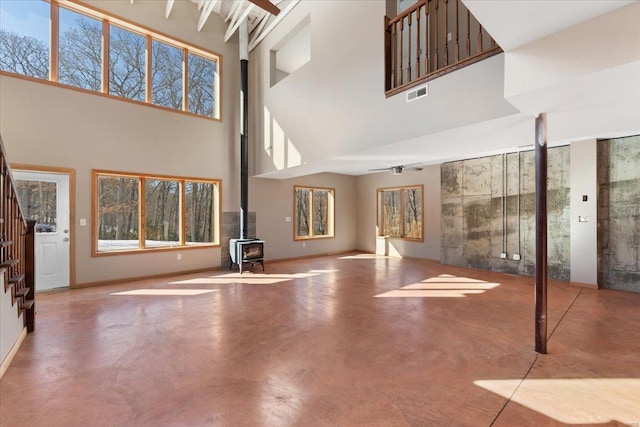 unfurnished living room with a wood stove, concrete floors, and a towering ceiling