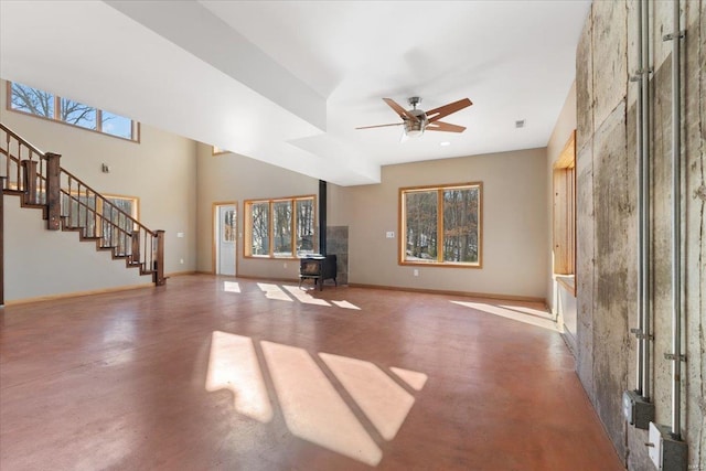 unfurnished living room with ceiling fan, concrete flooring, and a wood stove