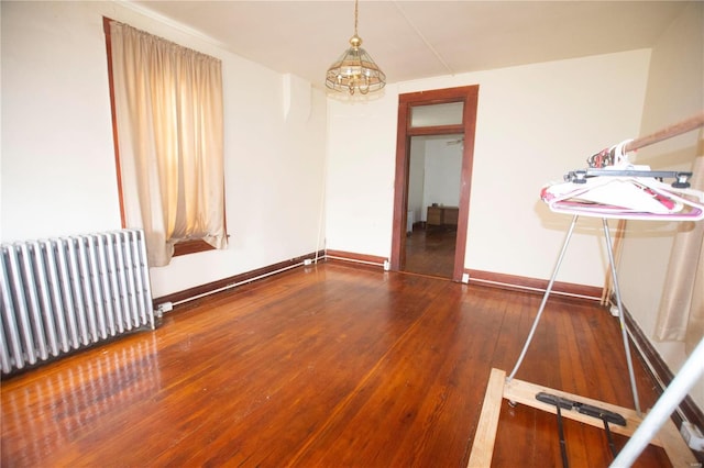 empty room with radiator heating unit, dark hardwood / wood-style floors, and a notable chandelier