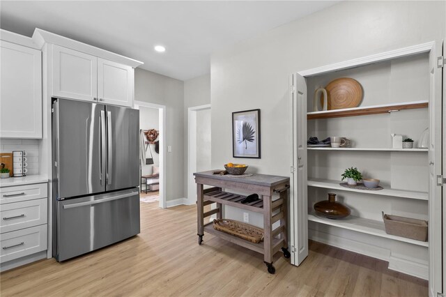 kitchen featuring tasteful backsplash, freestanding refrigerator, light wood-style floors, white cabinetry, and light countertops