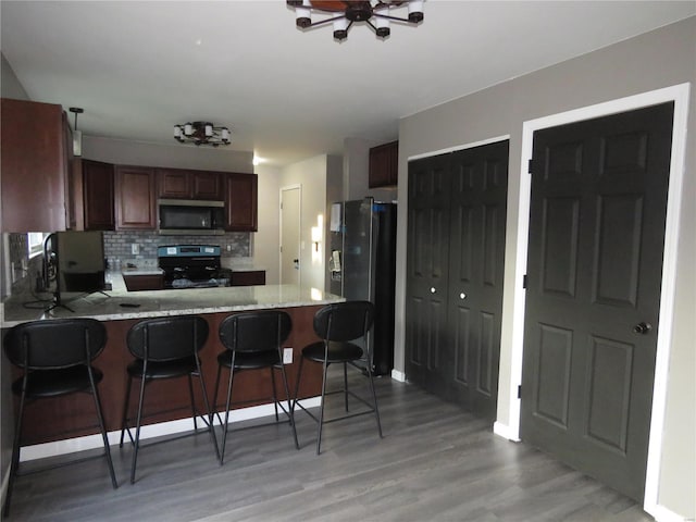 kitchen with black appliances, tasteful backsplash, kitchen peninsula, and light hardwood / wood-style flooring