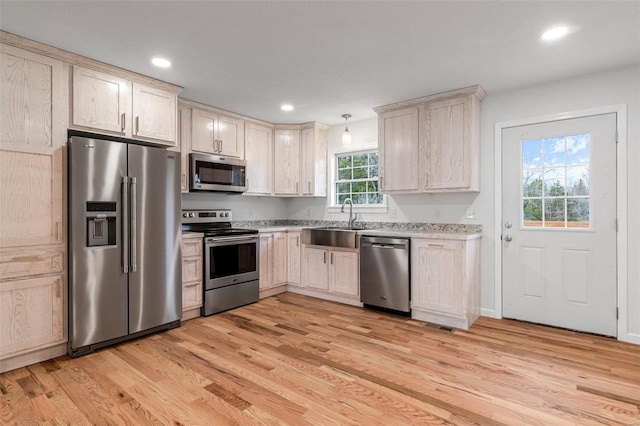 kitchen featuring sink, light wood-type flooring, hanging light fixtures, and appliances with stainless steel finishes