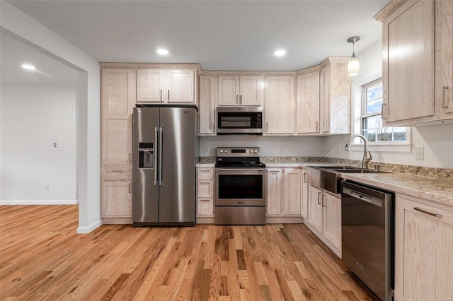 kitchen featuring sink, light brown cabinets, hanging light fixtures, stainless steel appliances, and light wood-type flooring