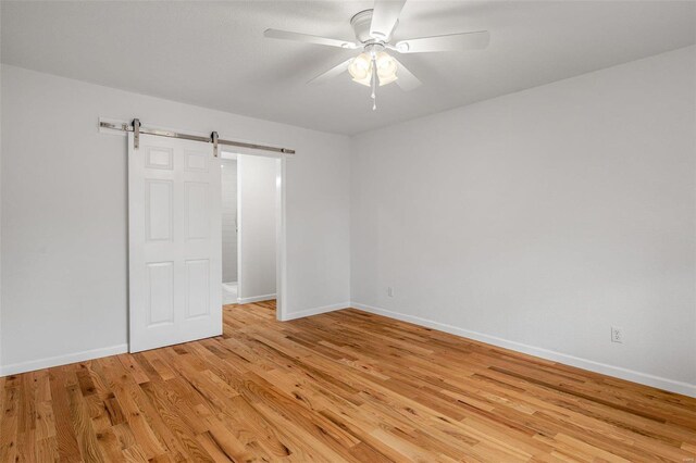 unfurnished bedroom with light wood-type flooring, a barn door, and ceiling fan