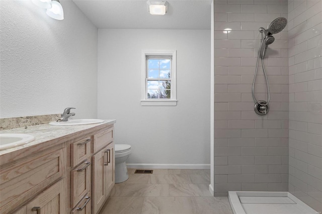 bathroom with a tile shower, vanity, and toilet