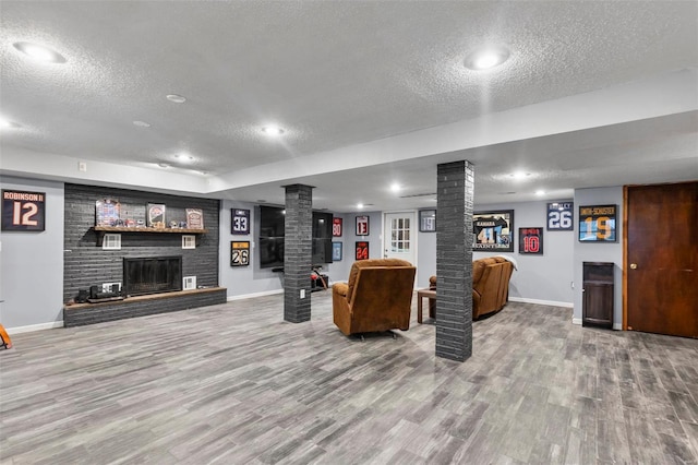 living room with a textured ceiling, a brick fireplace, wood-type flooring, and decorative columns