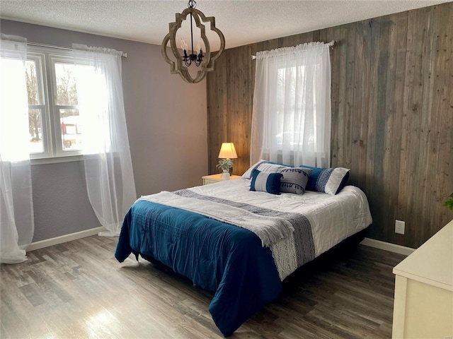 bedroom with an inviting chandelier, wooden walls, a textured ceiling, and dark hardwood / wood-style floors