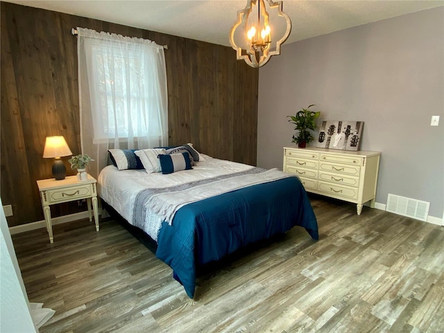 bedroom featuring wooden walls, a chandelier, and hardwood / wood-style flooring