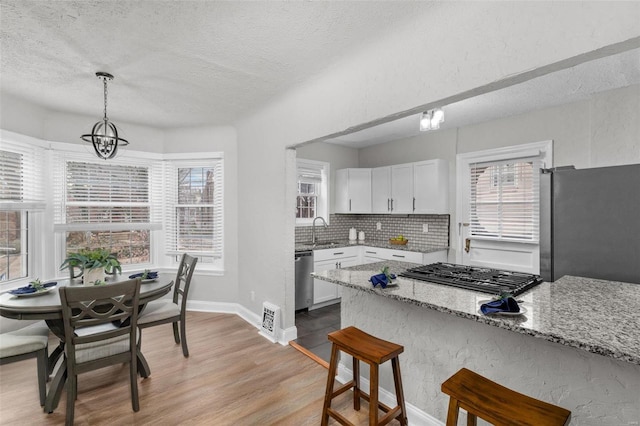 kitchen with light stone countertops, appliances with stainless steel finishes, decorative light fixtures, white cabinets, and light hardwood / wood-style floors