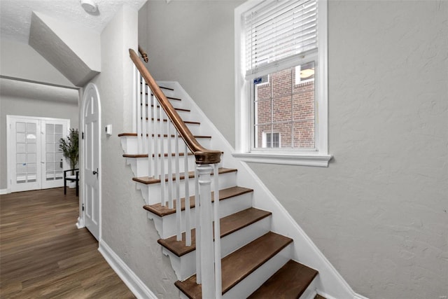 stairs featuring french doors, a textured ceiling, and hardwood / wood-style flooring