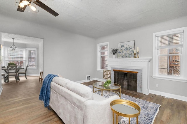 living room featuring ceiling fan, a fireplace, wood-type flooring, and a textured ceiling