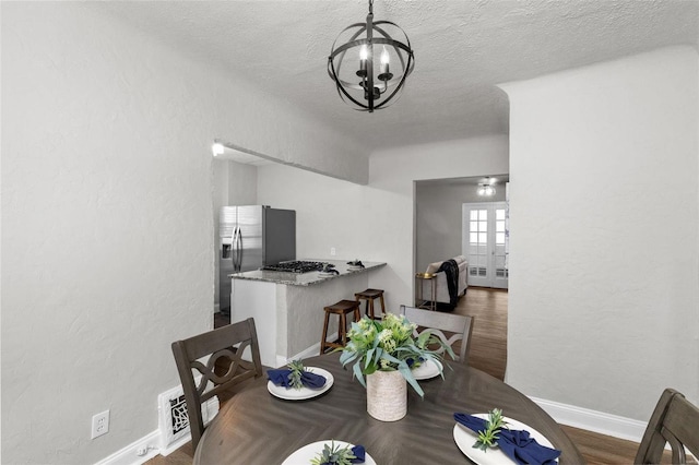 dining space featuring dark hardwood / wood-style floors, french doors, a textured ceiling, and a chandelier