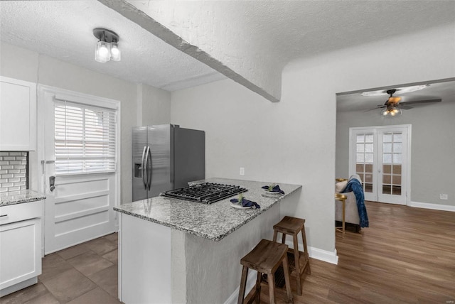 kitchen featuring white cabinets, a breakfast bar, kitchen peninsula, and stainless steel refrigerator with ice dispenser