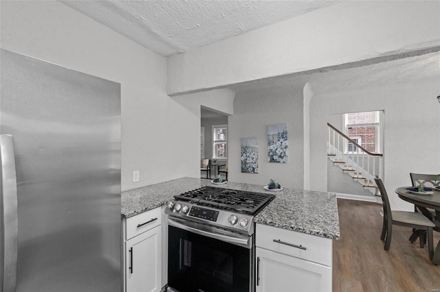 kitchen featuring kitchen peninsula, light stone counters, stainless steel appliances, hardwood / wood-style flooring, and white cabinets