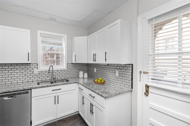 kitchen with white cabinetry, dishwasher, light stone countertops, sink, and dark tile patterned floors