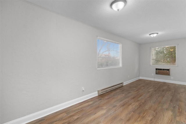 empty room featuring baseboard heating, a wealth of natural light, a wall mounted air conditioner, and hardwood / wood-style flooring