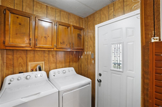 laundry room featuring cabinets, a textured ceiling, washing machine and dryer, and wooden walls