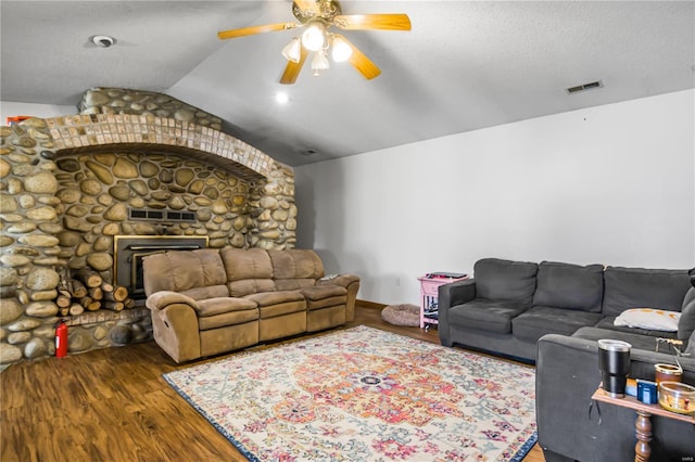 living room with a textured ceiling, dark hardwood / wood-style flooring, a stone fireplace, vaulted ceiling, and ceiling fan