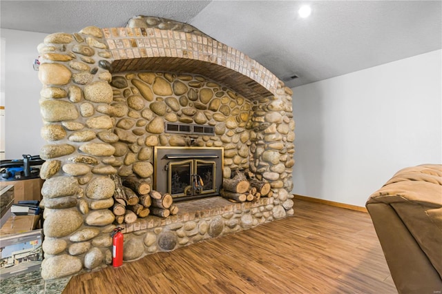 living room featuring lofted ceiling, a stone fireplace, a textured ceiling, and light hardwood / wood-style flooring