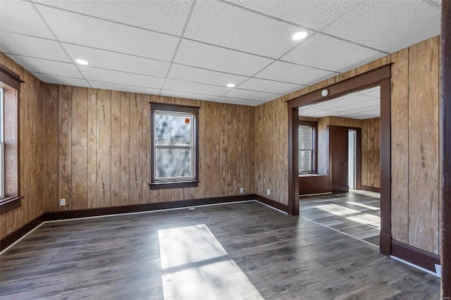 spare room with wood walls, a drop ceiling, and dark hardwood / wood-style floors