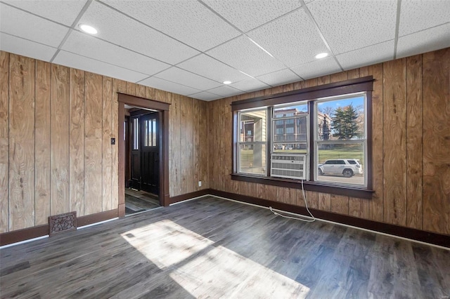 spare room featuring wooden walls, dark hardwood / wood-style flooring, and a drop ceiling