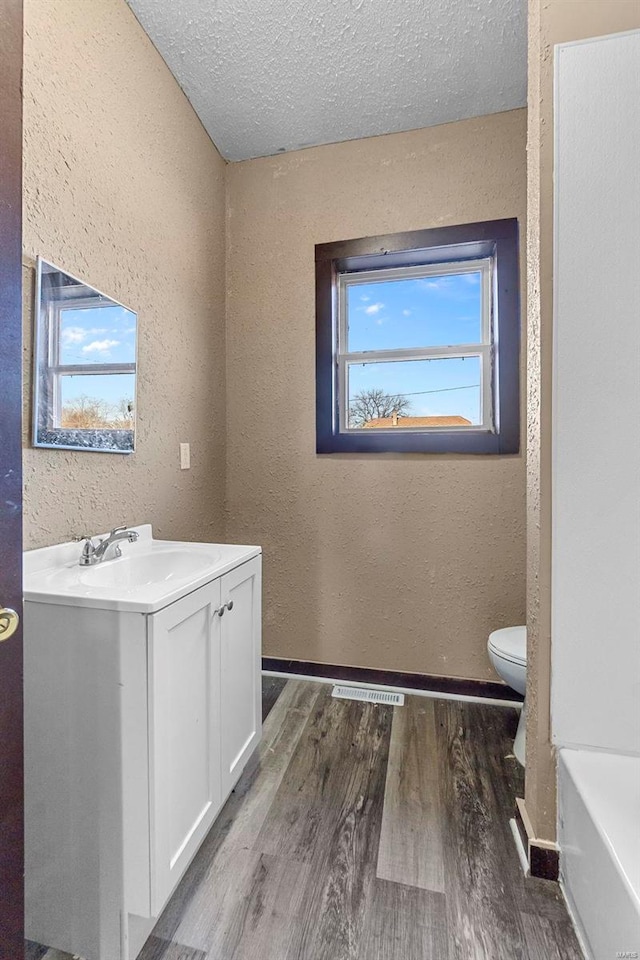 bathroom with hardwood / wood-style floors, vanity, a textured ceiling, and toilet