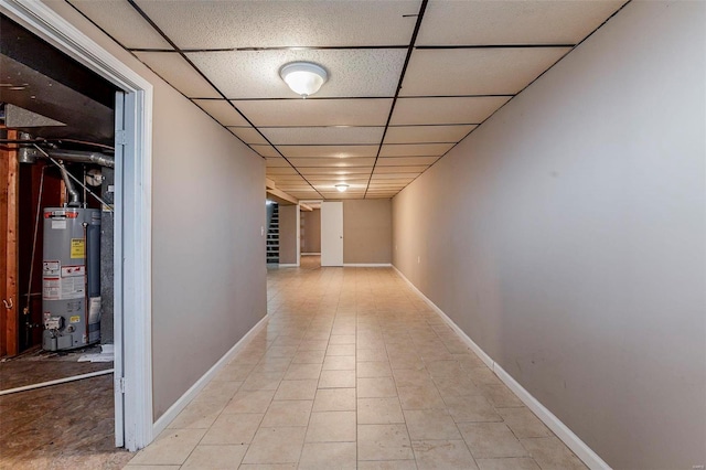 hallway featuring a drop ceiling, light tile patterned floors, and gas water heater