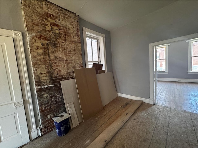 misc room featuring wood-type flooring, plenty of natural light, and brick wall