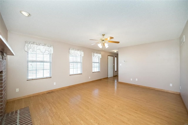 unfurnished room featuring a fireplace, ceiling fan, light hardwood / wood-style flooring, and a textured ceiling