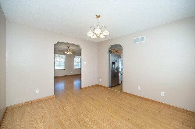 empty room with ceiling fan with notable chandelier and light hardwood / wood-style flooring