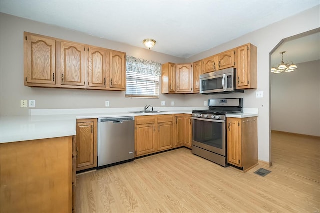 kitchen with pendant lighting, sink, a notable chandelier, light hardwood / wood-style floors, and stainless steel appliances