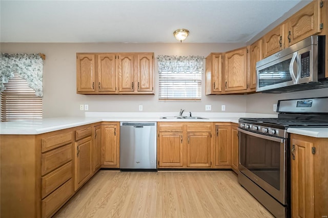 kitchen featuring kitchen peninsula, light wood-type flooring, sink, and appliances with stainless steel finishes