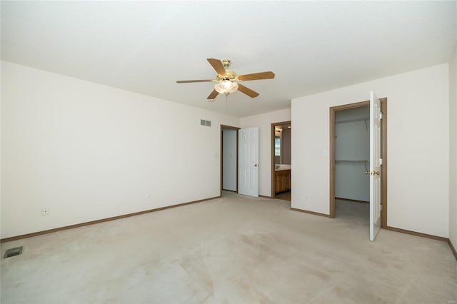 unfurnished bedroom with ensuite bath, ceiling fan, a spacious closet, light colored carpet, and a closet