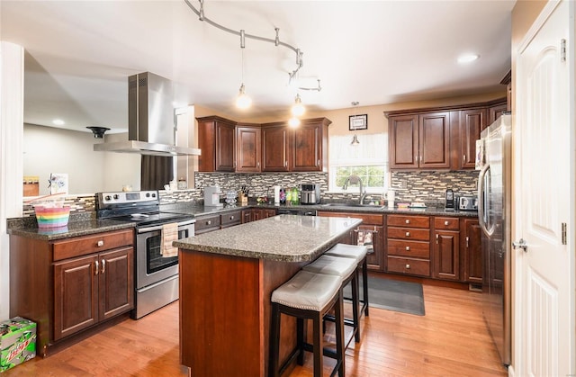 kitchen with a kitchen island, light wood-type flooring, stainless steel appliances, and range hood