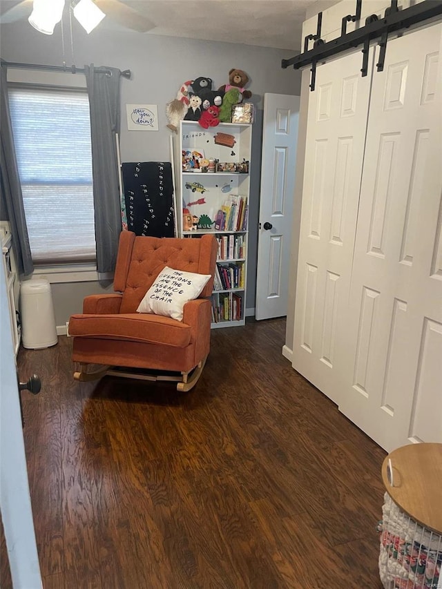 sitting room featuring a barn door, ceiling fan, and dark hardwood / wood-style floors