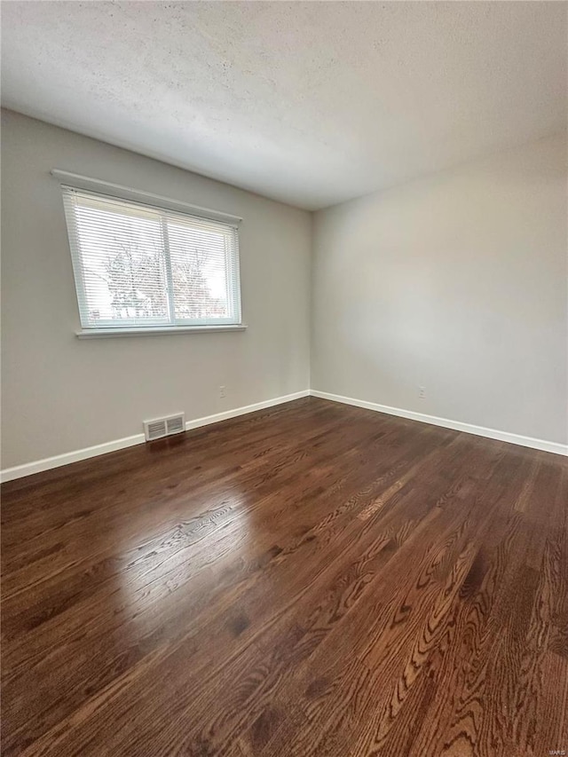 empty room with dark hardwood / wood-style floors and a textured ceiling