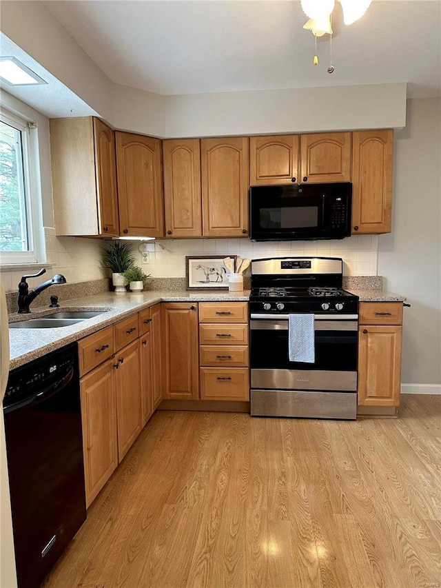 kitchen with backsplash, a skylight, sink, black appliances, and light hardwood / wood-style flooring