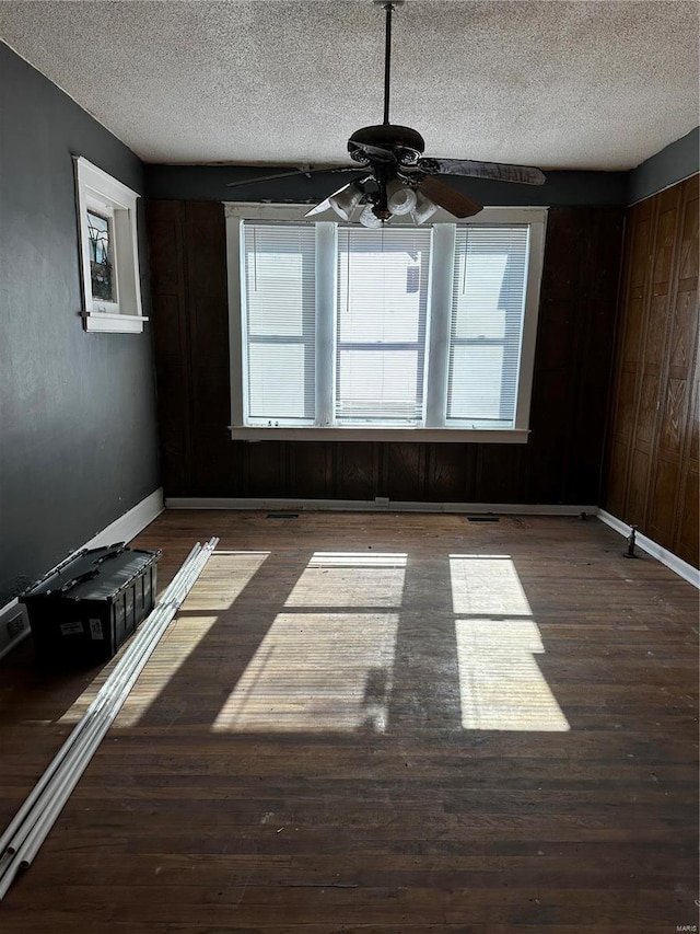 spare room featuring a textured ceiling, wooden walls, ceiling fan, and dark hardwood / wood-style floors