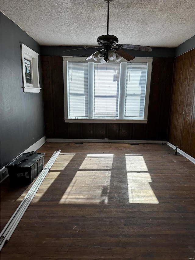 unfurnished room with a textured ceiling, dark hardwood / wood-style flooring, ceiling fan, and wood walls