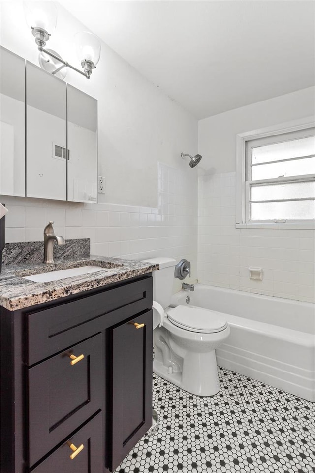 full bathroom with vanity, decorative backsplash, tiled shower / bath combo, toilet, and tile walls