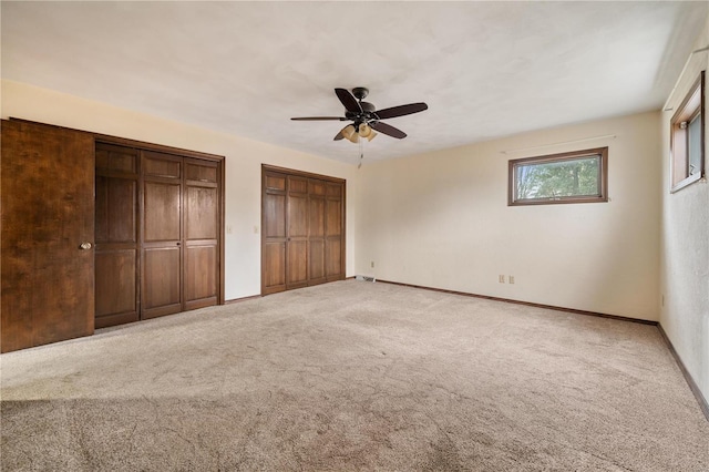 unfurnished bedroom featuring carpet flooring, ceiling fan, and multiple closets