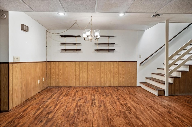 basement featuring wood-type flooring, a paneled ceiling, an inviting chandelier, and wooden walls